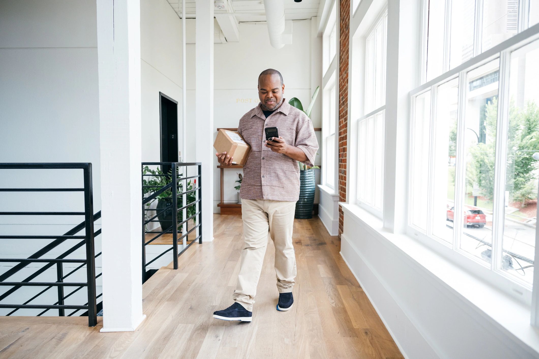 Customer receiving a delivery package while checking details on a phone